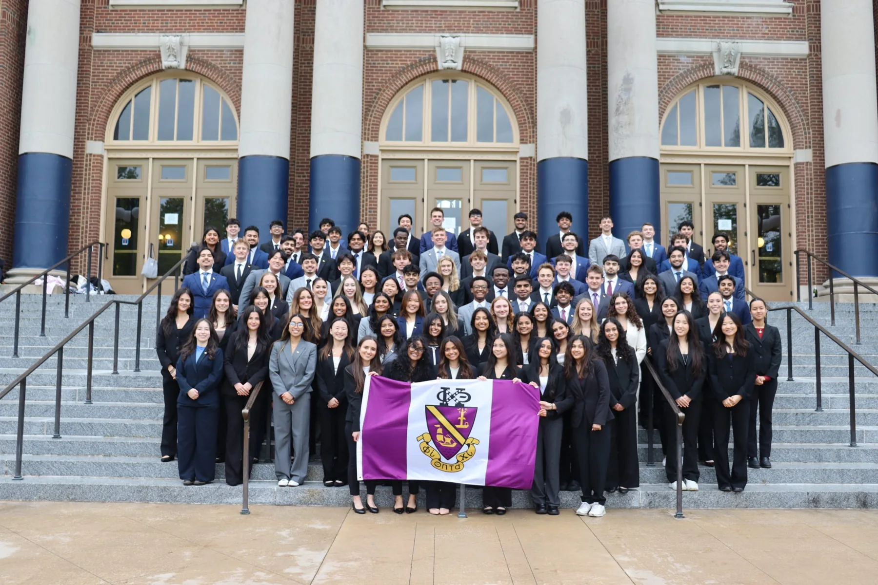 Phi Chi Theta chapter gathered outside with the chapter flag